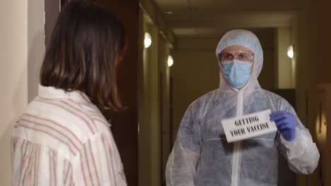 medical worker with text on paper visiting woman at home offering vaccination against coronavirus