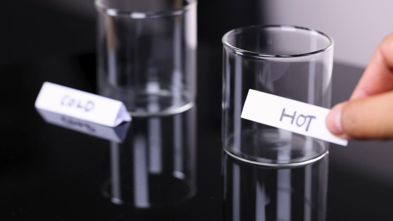 Hand labels empty glass as hot beside cold glass, under bright studio lighting, close-up shot