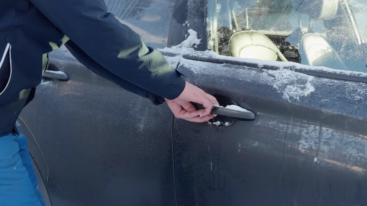 Man struggles to open passenger door of car frozen shut during winter in Norway.