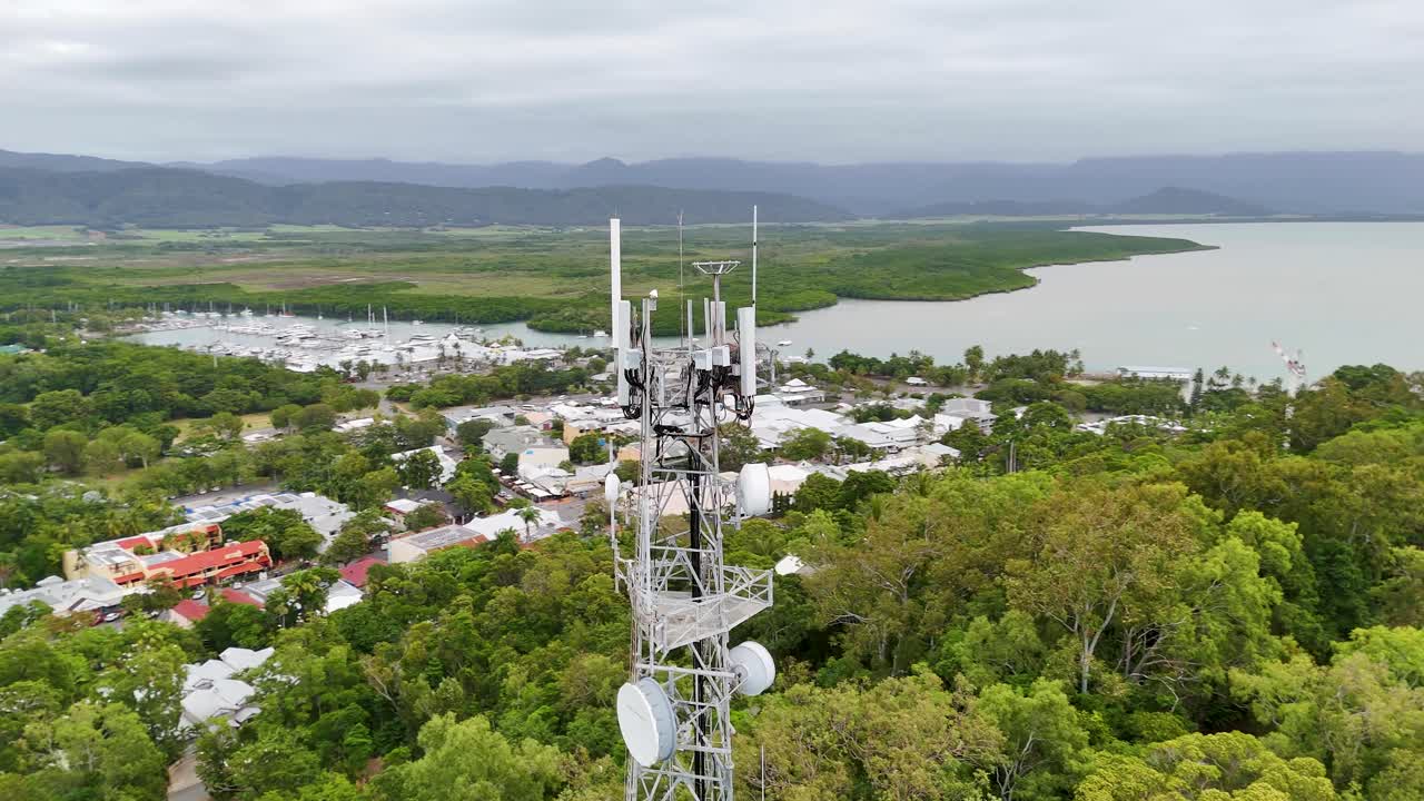 Drone footage captures a sweeping aerial view of Port Douglas, showcasing lush greenery, coastal waters, and a communication tower