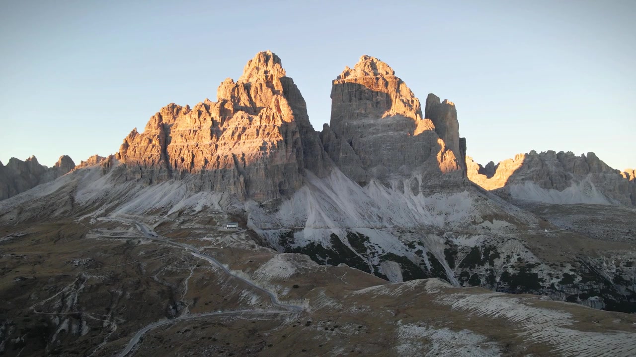 Calda luce solare che illumina le Tre Cime di Lavaredo, nelle Dolomiti italiane, durante un bellissimo tramonto, con rocce e creste in primo piano, Alto Adige, ripresa rivelatrice con drone al rallentatore.