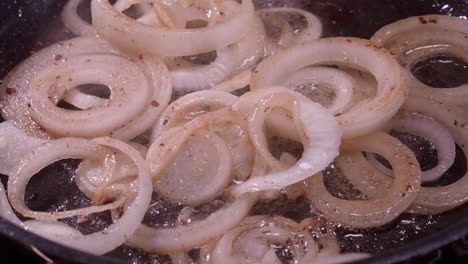 closeup: onion rings sizzle, sputter as they fry in hot frying pan oil