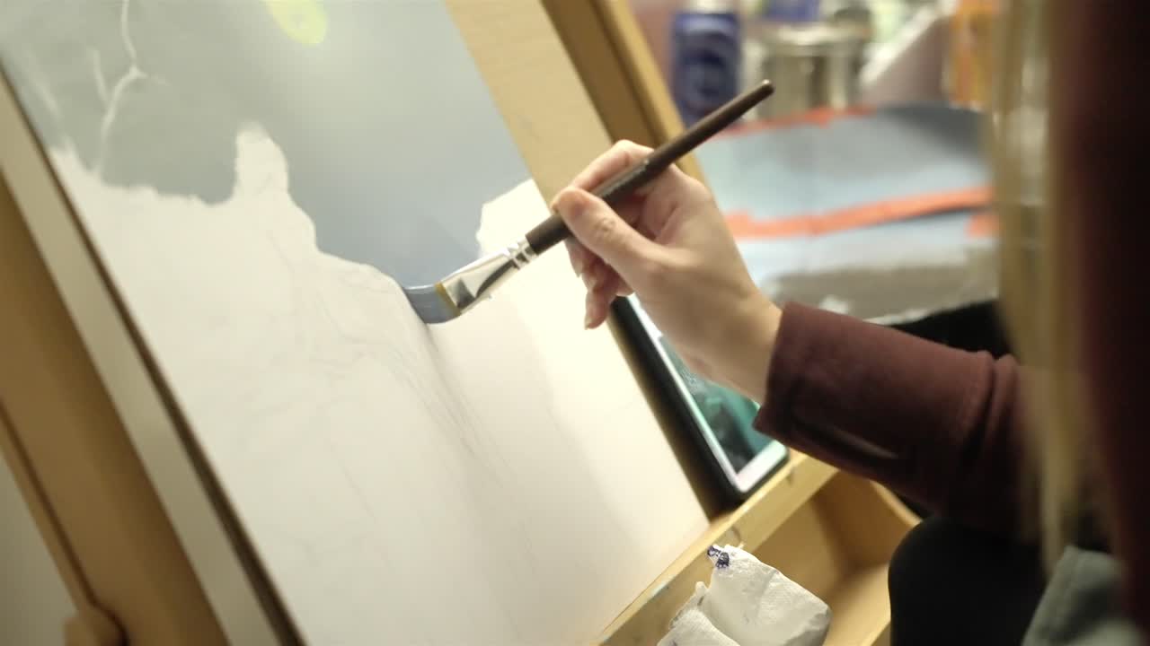 ศิลปินกำลังวาดภาพด้วยมือบนผืนผ้าใบด้วยพู่กันในสตูดิโอ ถ่ายแบบโคลสอัพ