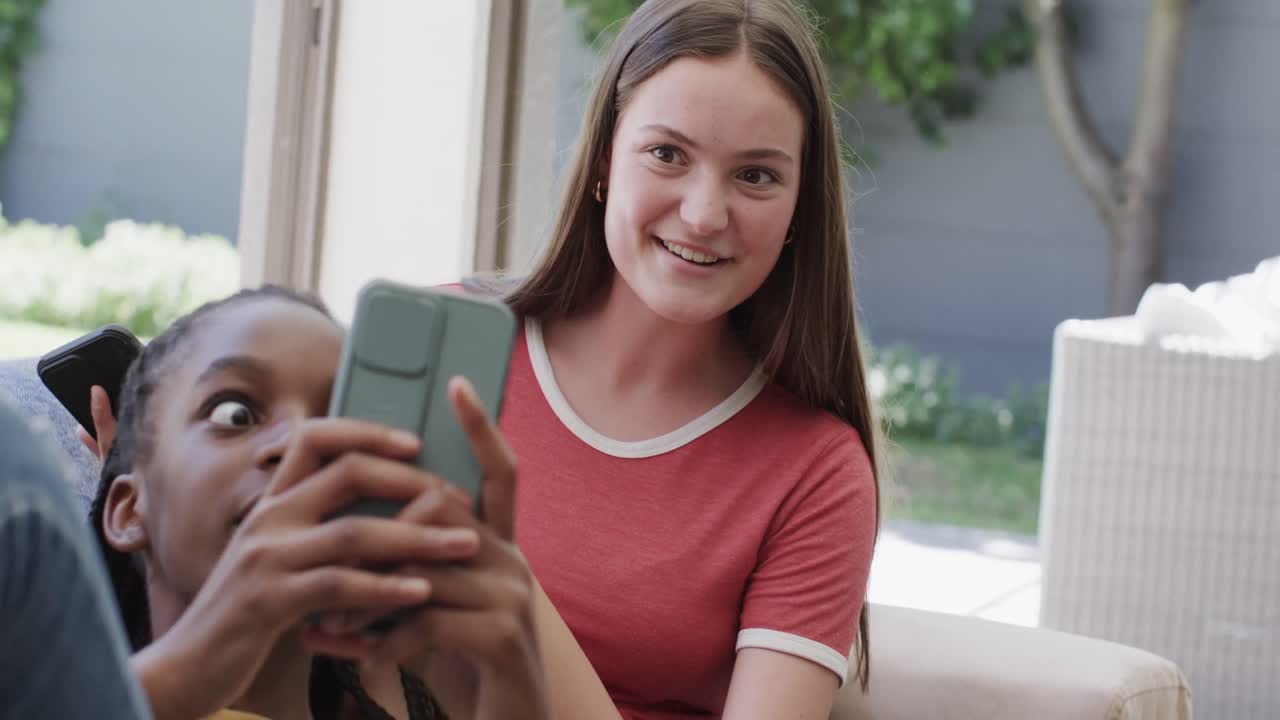sorprendidas diversas amigas adolescentes acostadas en el sofá y usando teléfonos inteligentes en cámara lenta