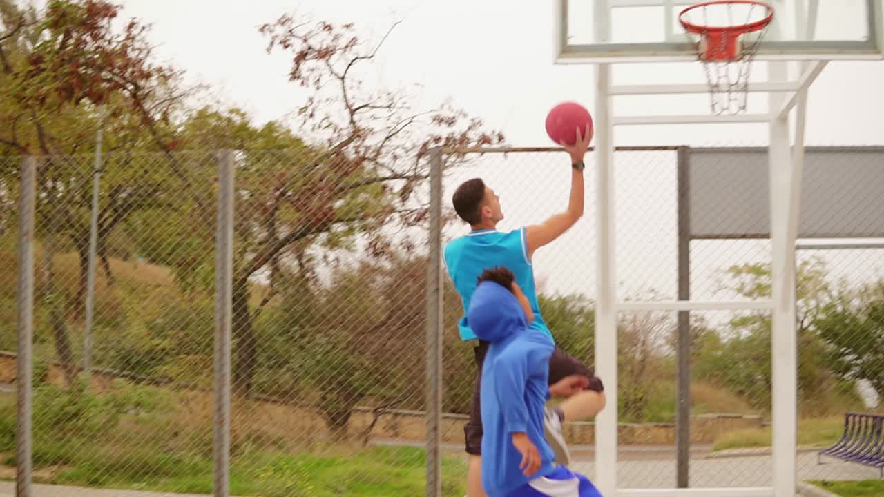 dos jóvenes amigos juegan al baloncesto en la calle. un tipo recibe una pelota en la canasta. disparo en cámara lenta