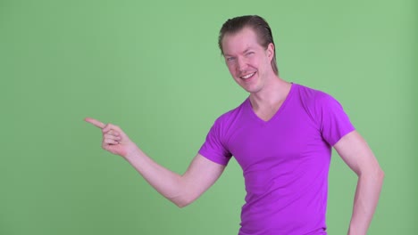 fotografía de estudio de un joven que parece emocionado mientras señala con el dedo para copiar el espacio contra un fondo verde
