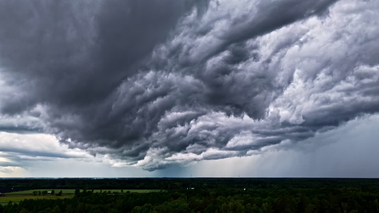 Static aerial shot of dark storm clouds forming above green countryside with a distant truck driving along a rural road in Latvia