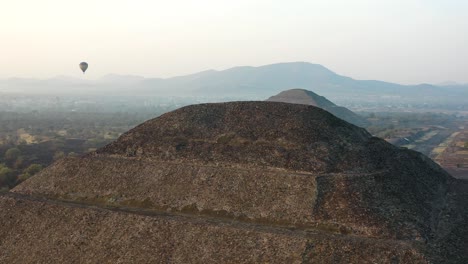 Vista-Aérea-Del-Globo-Aerostático-Volando-Entre-La-Pirámide-De-La-Luna-Y-La-Pirámide-Del-Sol-En-La-Antigua-Ciudad-Mesoamericana-De-Teotihuacan,-México-Desde-Arriba,-América-Central,-Amanecer,-4k