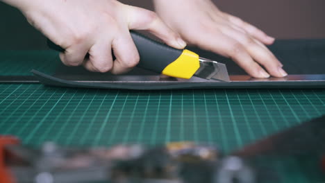 person cuts black leather fabric with special box cutter