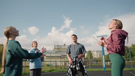 training session of beginners playing volleyball amongst themselves with coach wearing plaid shirt around waist in open court with basketball hoop and fence in background