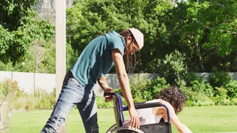 happy biracial woman in wheelchair dancing in garden with male partner with dreadlocks