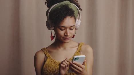 music app .young stylish cheerful african american lady wearing headphone choosing track on smartphone online