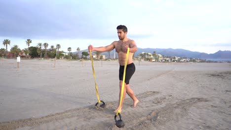 Stoffwechseltraining-Am-Strand-Mit-Muskulösem-Mann,-Der-Brust--Und-Gummivariante-Mit-Kettlebell-Macht