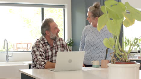 mature couple enjoying coffee and conversation at home with laptop nearby
