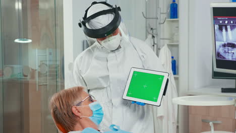 dentist in coverall pointing at green screen display in dental unit