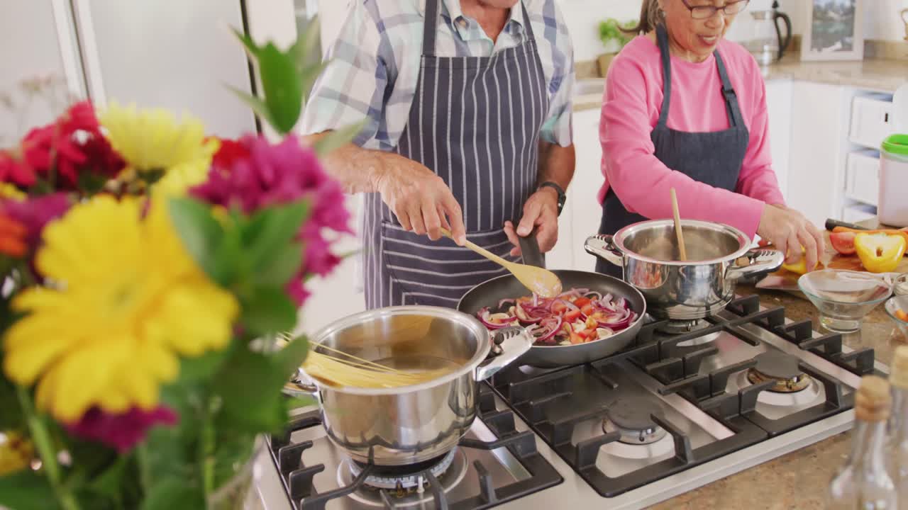 feliz pareja de ancianos diversos usando delantales y cocinando en la cocina