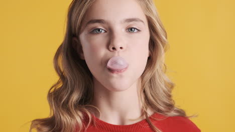 una adolescente caucásica masticando chicle y soplando burbujas.