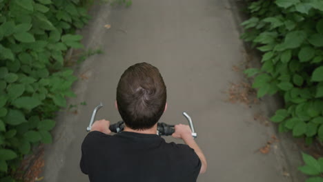 back view of someone cycling on a paved path with white markings, surrounded by lush roadside greenery, the cyclist pedals off, enjoying the scenic ride along the natural path