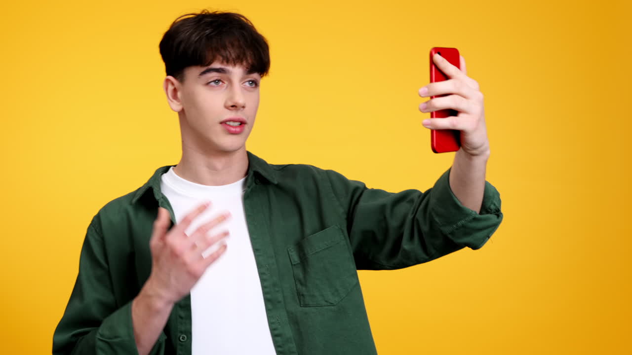 Giovane che parla mentre si filma al telefono e gesticola su sfondo giallo