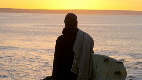 vista trasera de un hombre adulto con tabla de surf de pie cerca de la costa 4k