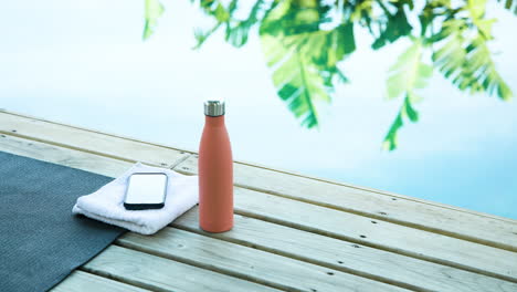 yoga mat, water bottle, and smartphone on deck by pool, tropical setting, copy space