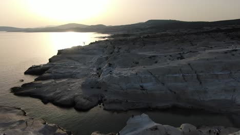 vista de avión no tripulado en grecia volando sobre una zona de roca blanca en forma de luna en la isla de milos al amanecer junto al mar azul oscuro