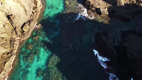 Flying-over-crystal-blue-waters-and-rocky-reef-breaking-onto-seashore-of-pacific-island