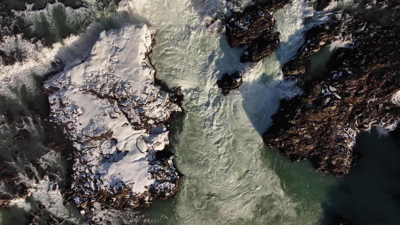 Snow-covered rocks in Urriðafoss, Iceland, with crashing ocean waves