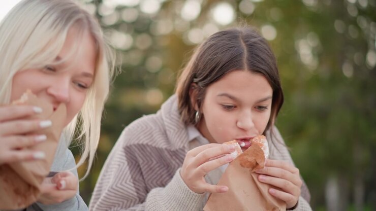 Due ragazze adolescenti che mangiano pasticcini all'aperto in un parco