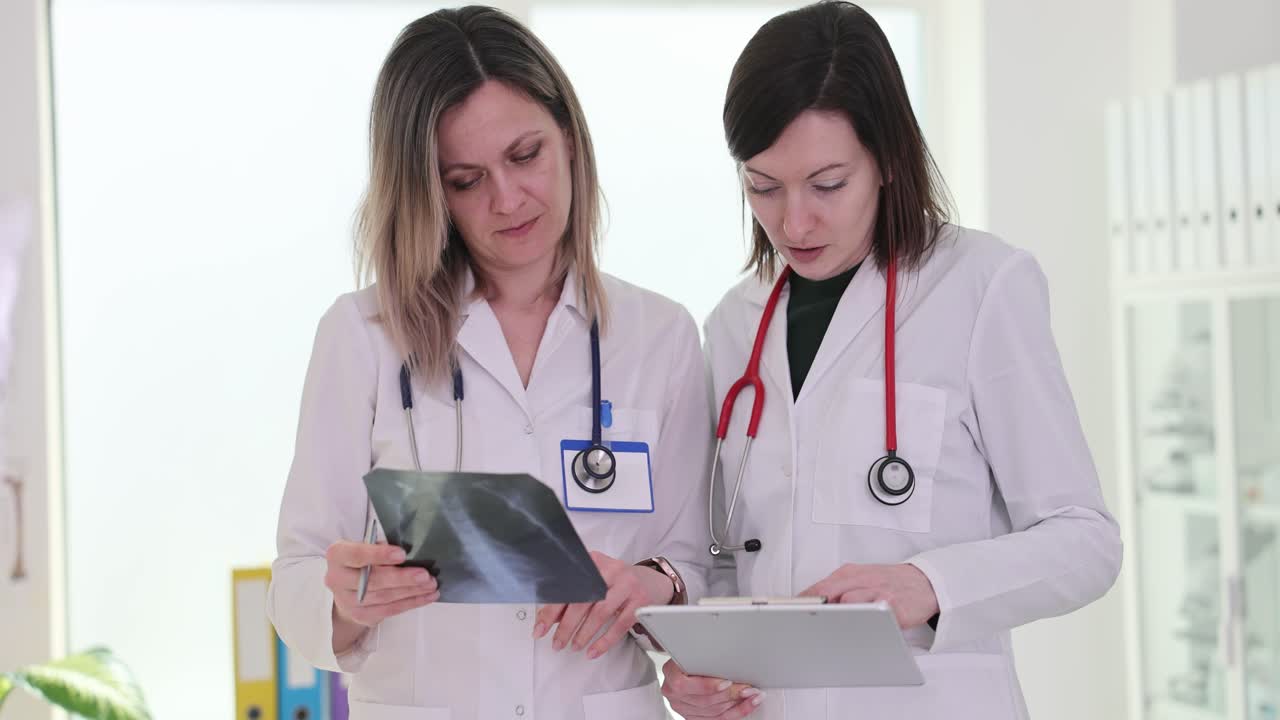 Two female doctors examining an X-ray and a tablet in a medical setting