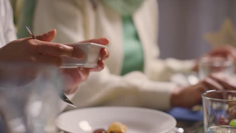 Close-Up-Of-Muslim-Muslim-Family-Sitting-Around-Table-At-Home-Eating-Meal-Together