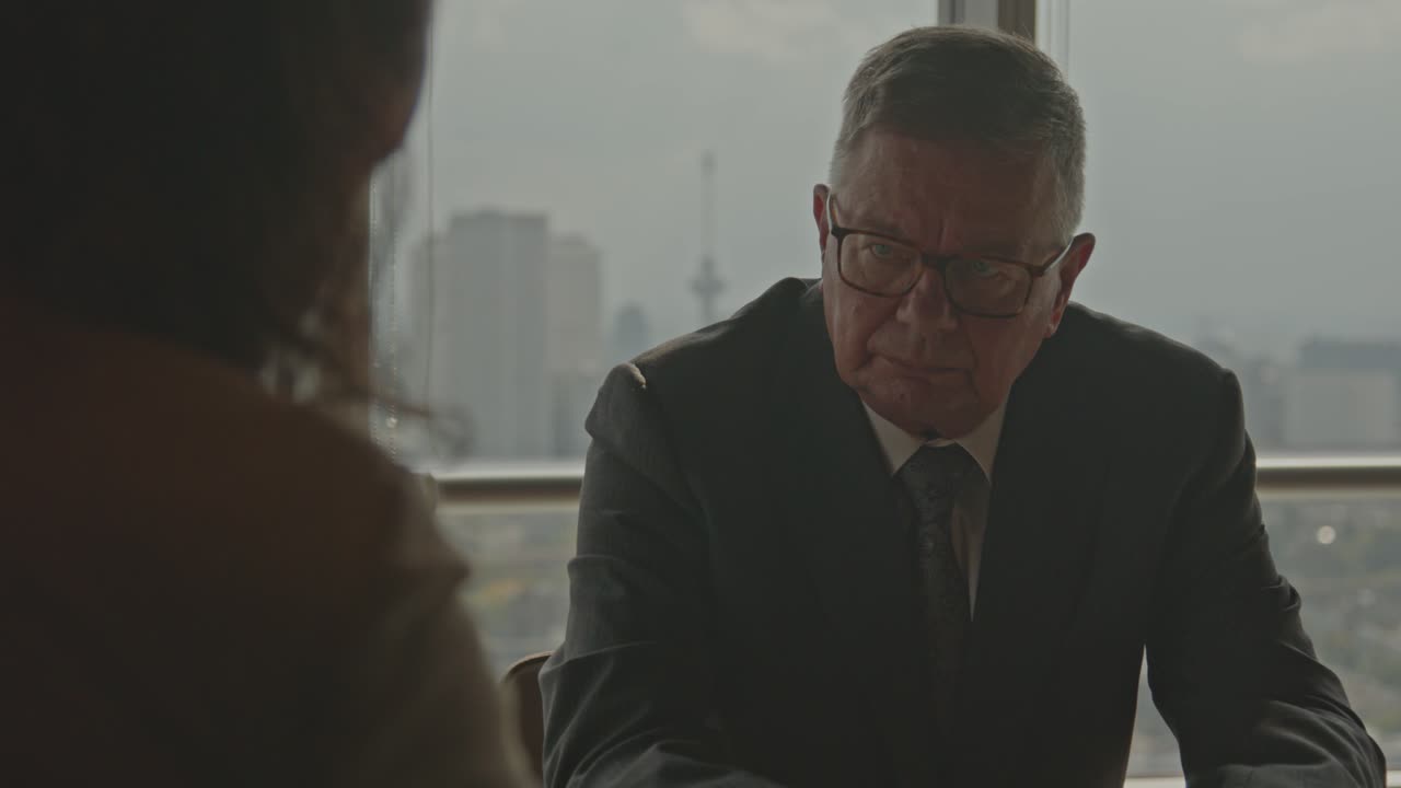 An older CEO talks to his business partner while sitting in a board roam