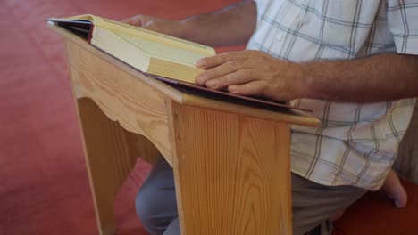 a muslim man kneeling and reading the quran