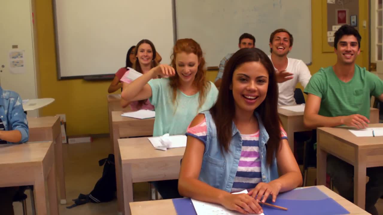 estudiantes riendo tirando papel en el salón de clases