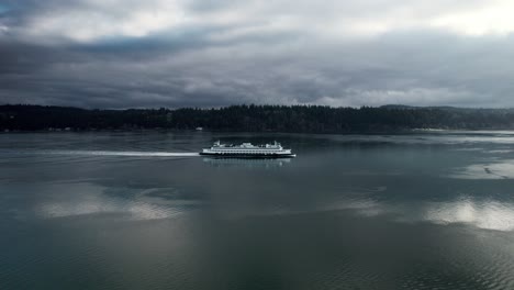 slowly tracking a commuter ferry as it cruises along a calm waterway reflecting dark gloomy clouds, aerial