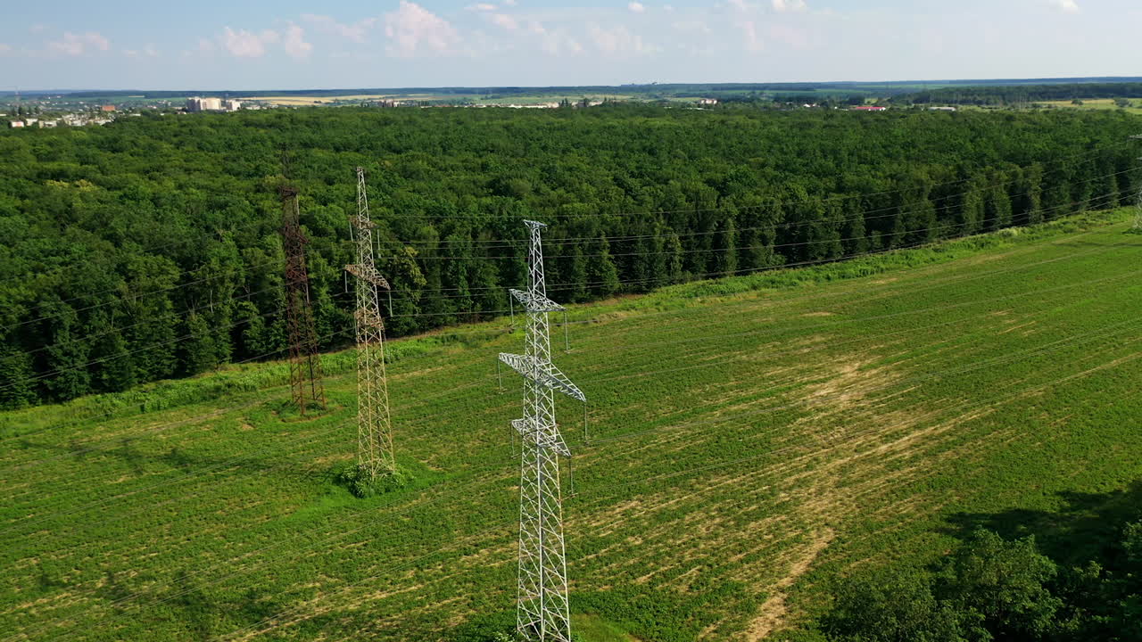 Transmission lines near green forest. High voltage electric line in the field. Steel pylons for electricity on beautiful nature background. Aerial view.
