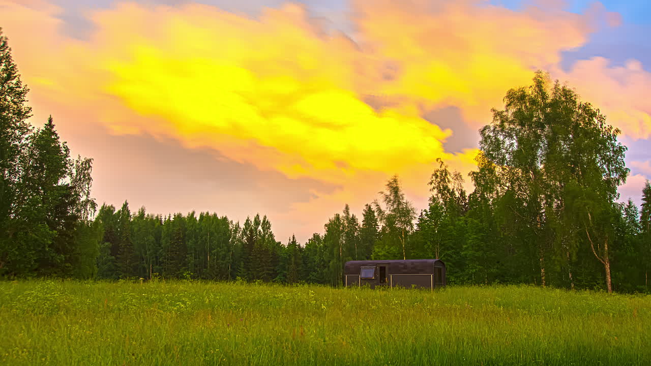 Thermowood-hytte i et smukt grønt landskab med skov i baggrunden - Farverige skyer, der flyver på himlen under solnedgang - 5K Timelapse-optagelse