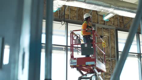 commercial construction worker raises and maneuvers man lift to work on duct.
