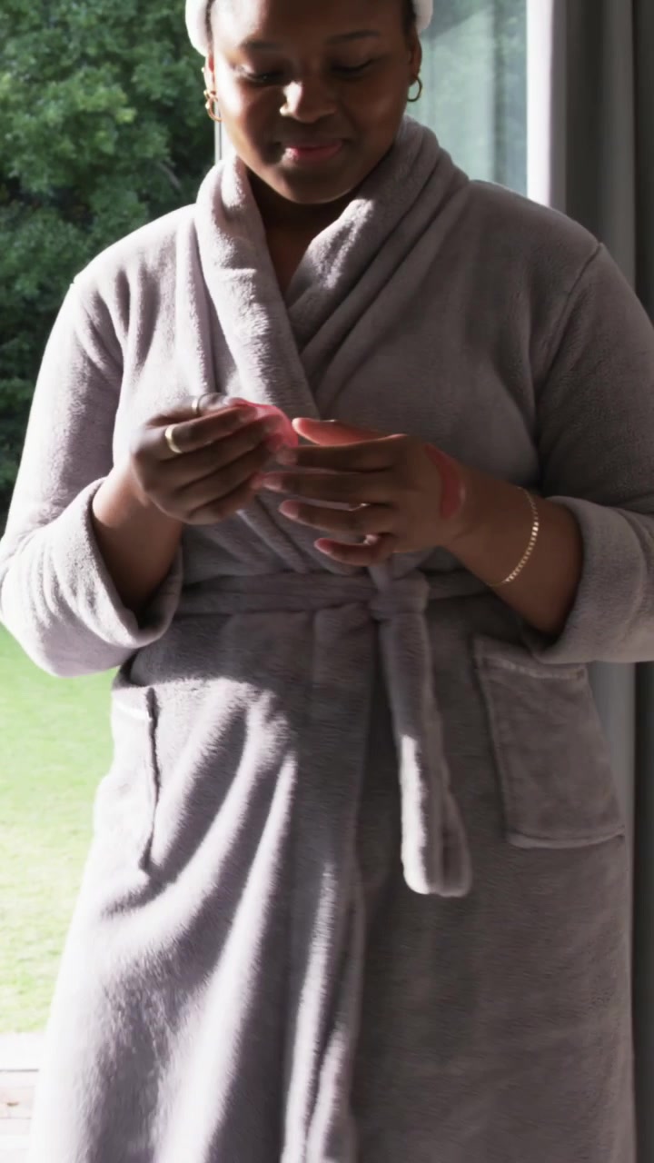 Vertical video: Noticing daylight, woman in grey bathrobe opening pink box by sliding glass door