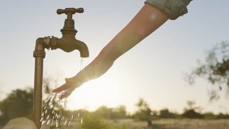 mujer lavando la mano bajo el grifo con agua dulce en tierras de cultivo rurales al amanecer