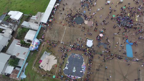 Rising-up-above-field-with-giant-kites-at-Sumpango-Kite-Festival,-aerial