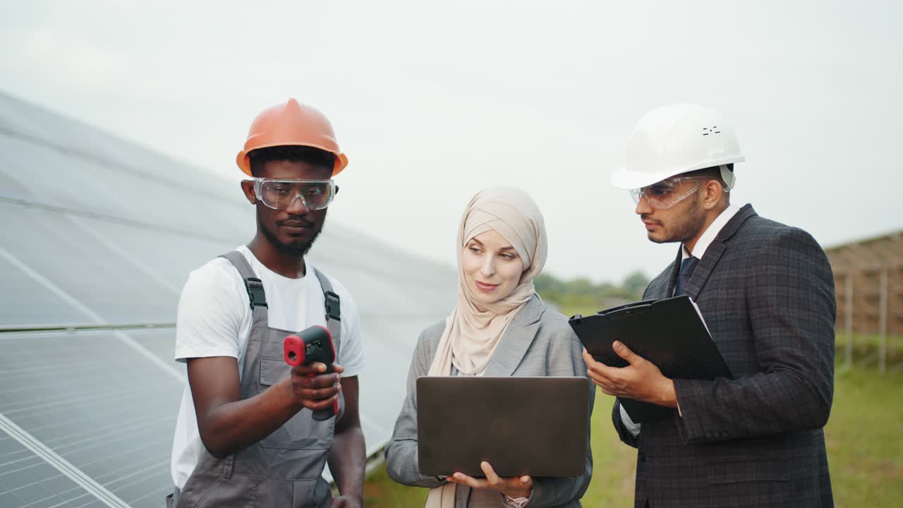 personas multirraciales controlando la temperatura de los paneles solares. trabajador industrial mostrando la imagen térmica con índices a los inspectores. inspección en la estación solar