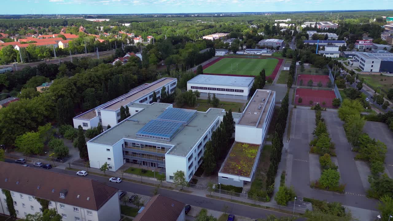 Hennigsdorf High School showcasing its modern architecture, sports facilities, parking area, surrounding urban landscape. Stunning aerial view flight panorama orbit drone