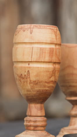 carved wooden goblets on table in yard against fence. medieval tableware made of natural materials. handcrafted drinkware on blurred background