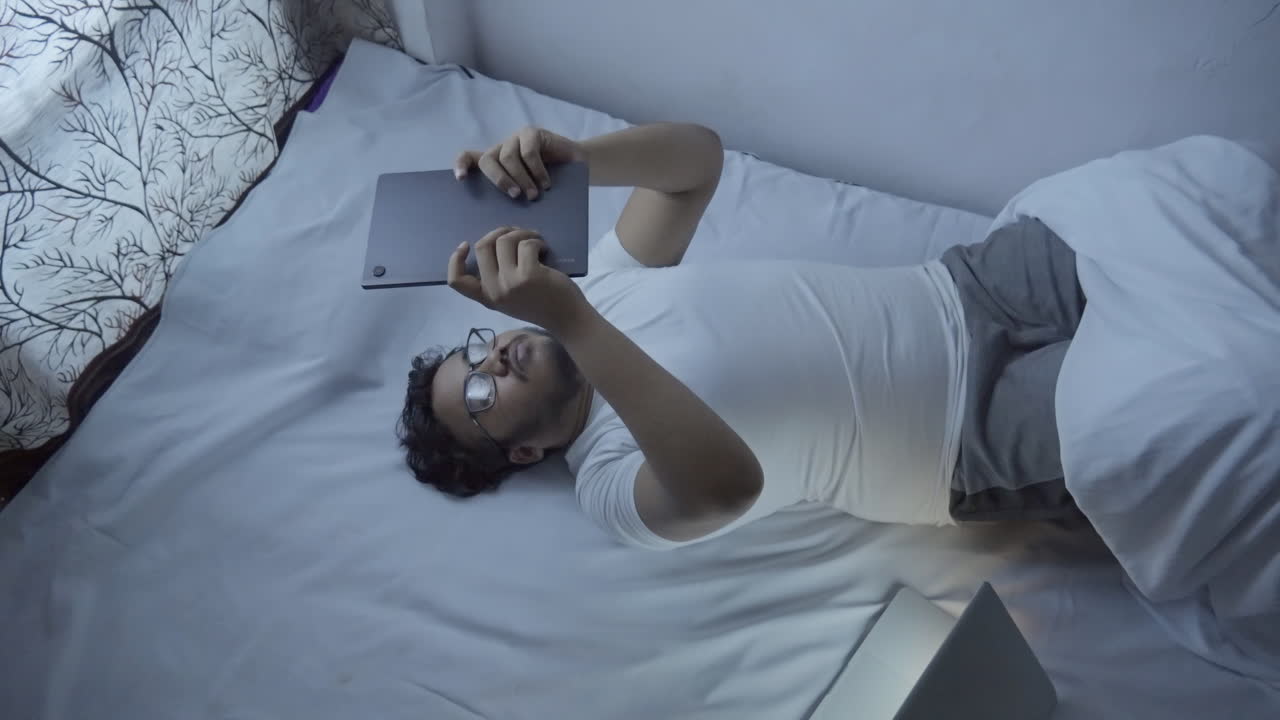 늦은 밤에 디지털 태블릿을 사용하여 침대에 누워있는 인도 젊은 남자의 상단 뷰