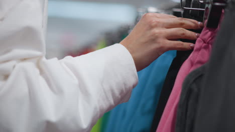 young woman browsing vibrant clothing rack in retail store, gently inspecting colorful garments with precision and attention to detail, brightly lit environment