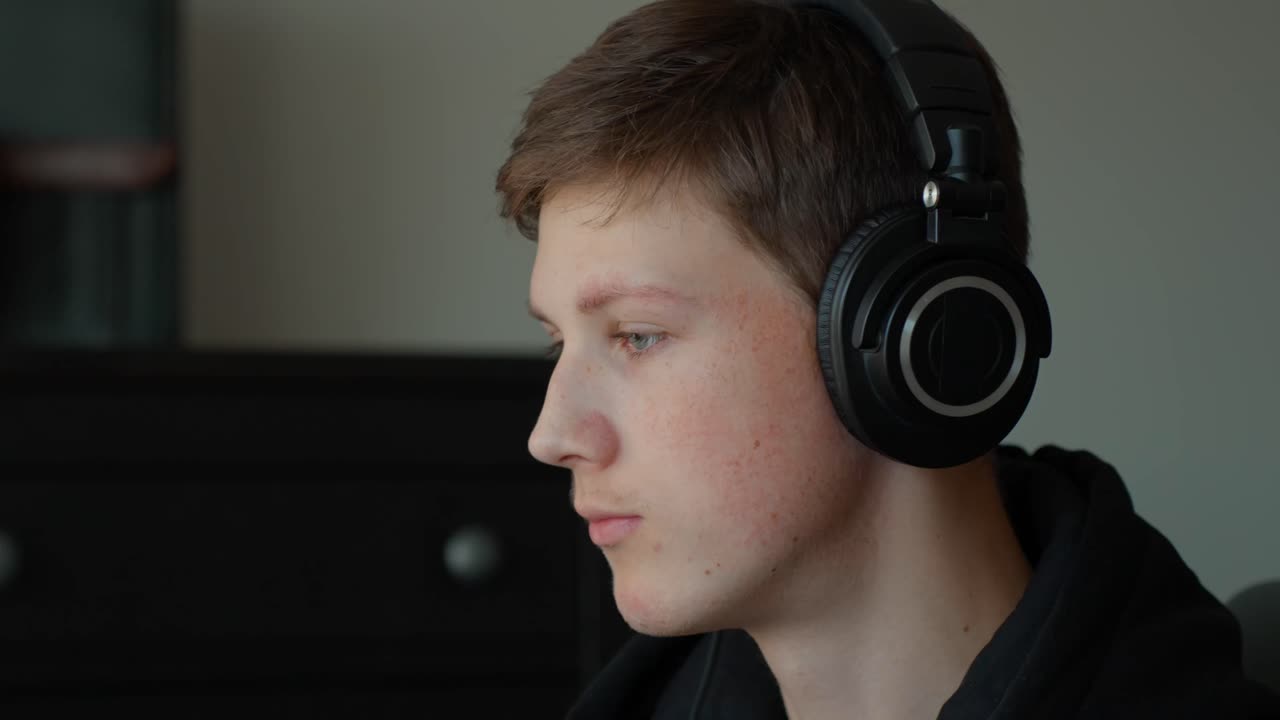 Mladý bělošský hudební producent se soustředí, poslouchá zvuk přes sluchátka, pracuje na mixování a masteringu audio stop v domácím nahrávacím studiu, vytváří nový zvuk a pak si je sundává.