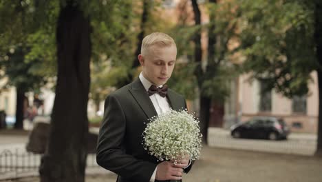 el novio de pie en el callejón del parque con un ramo de bodas esperando a su amada novia, primera reunión
