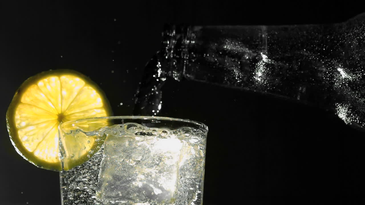 Bottiglia che versa acqua in un bicchiere con ghiaccio e una fetta di limone.