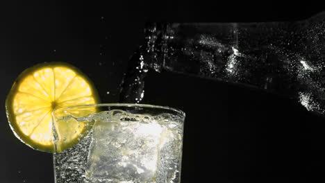 Bottle-pouring-water-into-glass-with-ice-and-lemon-wedge